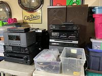 Overall lot of stacked audio electronics and plastic bins with cables on folding tables.