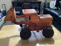 Photo showing the left side of the vintage Lincoln Construction Front End Loader metal tractor, highlighting the loader attachment, tires, and orange paint with wear.