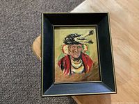 Framed small oil painting showing a portrait of a Native American chief in traditional clothing and feathered headdress, set on a table.