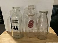 Three vintage milk bottles displayed side by side showing labels and shapes.