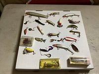 Top view showing all 22 fishing lures arranged on white board with some in original packaging.