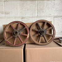 Two wooden and metal cart wheels side by side on cardboard boxes, showing size and overall look.
