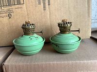 Pair of small green antique oil lamps showing front view and detailing on wick knobs and brass tops.