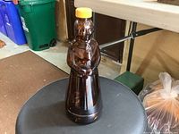 Front view of vintage brown glass bottle shaped like Aunt Jemima figure with yellow lid.