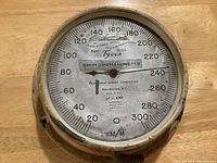 Front view of the vintage brass sphygmomanometer showing dial with measurement markings and manufacturer information.