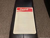 Full view of Coca-Cola menu sign showing white lined writing area and red Coca-Cola header.