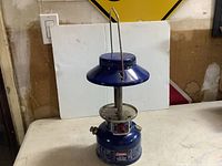 Front view of vintage Coleman lantern showing blue metal construction, carrying handle, and absence of glass.