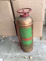 Side view of copper foamite fire extinguisher showing red handle and attached hose.