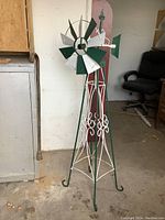 Full view of the vintage garden windmill standing on concrete floor indoors showing green and white painted metal structure with fan blades at top.