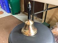 Side view of the vintage brass hand bell with black wooden handle and brass finial on top.