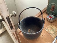 Front angled view of vintage cast iron pot with handle on wooden surface.