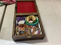 Wooden box with red velvet interior holding several bracelets of different colors and materials.