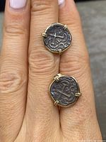 Front view of both earrings on fingertip showing coin faces and gold prong setting