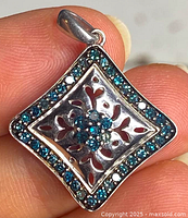 Close-up of sterling silver pendant held in hand showing blue diamond cluster and intricate cutout design.