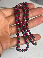 Necklace held in hand showing round alternating ruby and emerald beads with small gold spacers and 10K gold clasp.