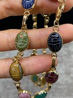Close-up of scarab stones showing green, yellow-brown, dark blue, and red stones with engraved scarab motifs, gold-filled linking elements visible