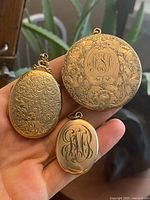 Photo of front side of 3 antique lockets showing floral and monogram engravings