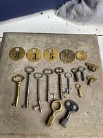 Full view of skeleton keys, winding keys, and brass numbered tags laid flat on surface.
