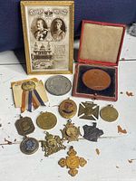 Wide shot of the full collection of antique coronation related medals, pins, coins, and framed postcard laid out on a surface.
