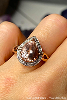 Ring worn on finger showing top view of pear-shaped morganite and surrounding diamond halo