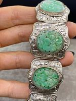Detail of three oval carved green jade panels set in ornate engraved silver rectangular links