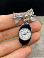 Front view of bow brooch suspending pendant watch, showing dial and enamel front