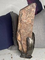 Full view of large hand-made Brutalist sculpture showing irregular brown stone and dark metal base with welded details.