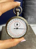 Front view of war era compass showing white dial with black and red numbering, inner dial, and two hands.