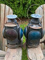 Front and side view of both lanterns on wooden chair, showing colored lenses and overall condition