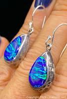 Close-up photo of teardrop-shaped sterling silver earrings with blue and green genuine opal inlays held by hand.