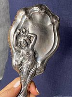 Close-up of back of the brush showing detailed Art Nouveau female figure design in solid sterling silver with tarnishing and patina.