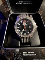 Swiss Military wristwatch face close-up inside original box showing brand, water resistance of 200M, black dial with date and metallic bracelet.