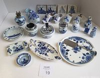 Photo of entire lot showing multiple Delft pottery pieces including plates, shoes, ashtrays, figurines, smoking set, and tiles arranged on a white surface