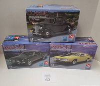 Three boxed AMT ERTL model car kits: Classic 1936 Ford Coupe, Muscle 1971 Dodge Charger R/T in yellow, and Muscle 1967 Mustang GT Fastback in black. Kits displayed unopened with boxes mostly intact, Mustang box torn.