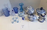 Full assortment of blue glass and pottery items on white table including dishes, vases, pitchers, liqueur glasses and figurines.