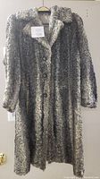 Front view of the silver and grey Persian lambswool coat hanging on a hanger showing button closure and two pockets.