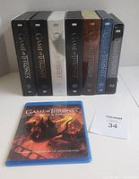 Boxed sets of Game of Thrones Seasons 1 to 7 on DVD and Blu-ray arranged vertically along with a separate blu-ray case of Conquest & Rebellion in front.
