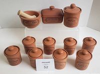 Photo showing the full set arranged on a white platform including mortar and pestle, butter box, honey jar, eight spice jars with labels, and salt keeper not shown in this photo.