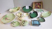 Lot overview showing all Carlton Ware pieces in various colors and patterns including green, dark green with gold, blue, yellow floral, and boxed small divided dish with spoon and cutter.