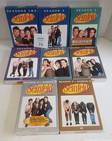 Front view of Seinfeld DVD seasons 1 & 2, 3, 4, 5, 6, 7, 8, and 9 box sets, showing cast photos and colorful covers. Seasons 4 and 8 are sealed.
