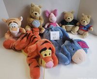 Seven Winnie the Pooh character stuffed animals grouped together showing Tigger, Eeyore, Piglet, Pooh with honey pot, and two GUND Classic Pooh bears wearing sweaters.