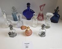 Overview of 11 assorted perfume bottles and atomizers arranged on a white surface, showing variety of shapes and colors including clear, blue, red, and pink.