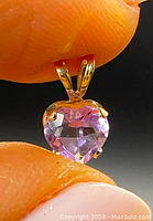 Close-up image of heart-shaped amethyst gemstone pendant held between fingers, showing the 14k gold setting and bail.