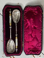 Two antique presentation spoons displayed in a fitted black box lined with maroon velvet and satin.