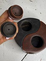 Two clay lids held above black and red yin-yang teapot halves showing underside of lids and openings.