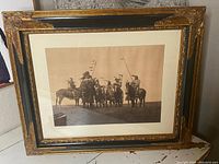 Front view of the framed photograph showing Native American men on horseback with spears and flags, set in an ornate gold and black frame.