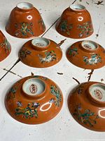 Seven upside down porcelain bowls showing the orange glazed outer surface with floral decoration and the white base marked "CHINA".