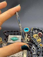 Hand holding silver-tone bar brooch with blue enamel and clear stones in front of assortment