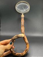 Full view of the magnifying glass held to show the burl wood handle and gold mount