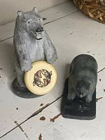 Overview of both soapstone bear sculptures on table, showing standing bear with disc and bear over fish